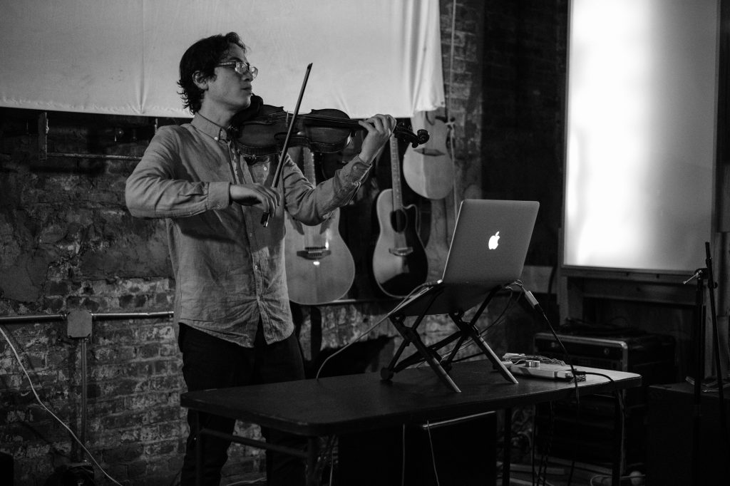 Black and white photo of Jeffrey Young performing at Spectrum in Brooklyn on violin and laptop