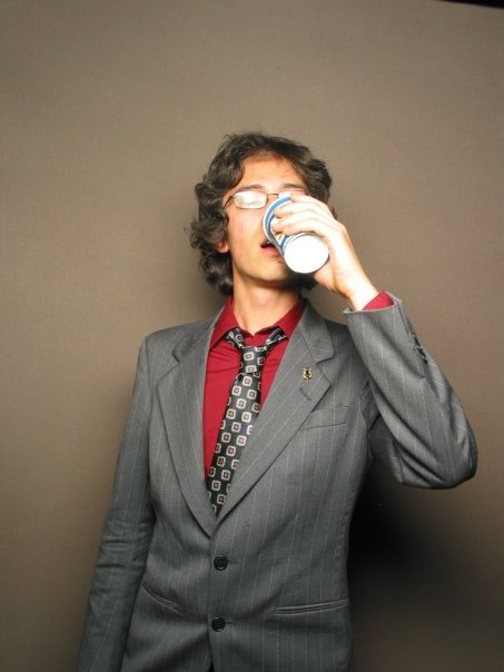 Jeffrey Young wearing a suit and tie, eyes closed, drinking from an old-fashioned NYC disposable deli coffee cup, in a photobooth shot