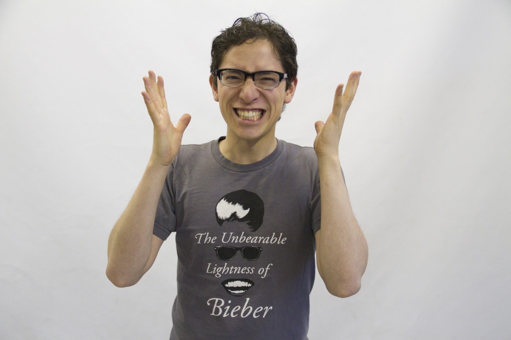 Jeffrey Young smiling manically at the camera, wearing a shirt that says The Unbearable Lightness of Bieber that also includes elements of Justin Bieber's face